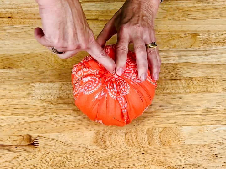 Pull the fabric up around the pumpkin, tucking it into the center. Create gathers and folds for texture.