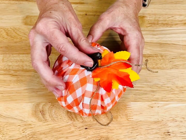 Attach the stem that comes with the pumpkin or create your own stem using a cinnamon stick, paper bag, or any other material. Use hot glue to secure it. Optionally, glue faux leaves around the stem.