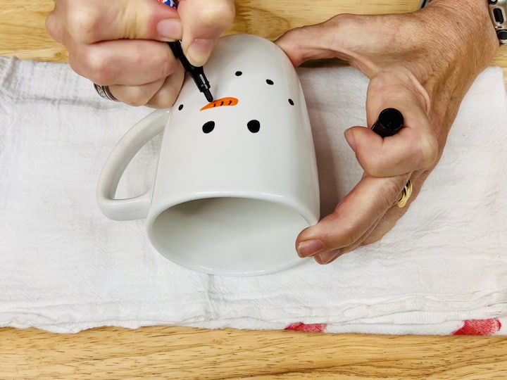 Step 3: Create Snowman Eyes Using the black paint pen, carefully draw two snowman eyes on the mug. Fill them in with the black paint to ensure they stand out against the mug's surface.