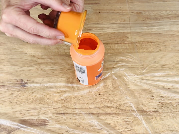 Pour the orange paint into one of the candle holders and swirl it around until the entire inside is coated. Dump out the excess paint back into the bottle for future use.