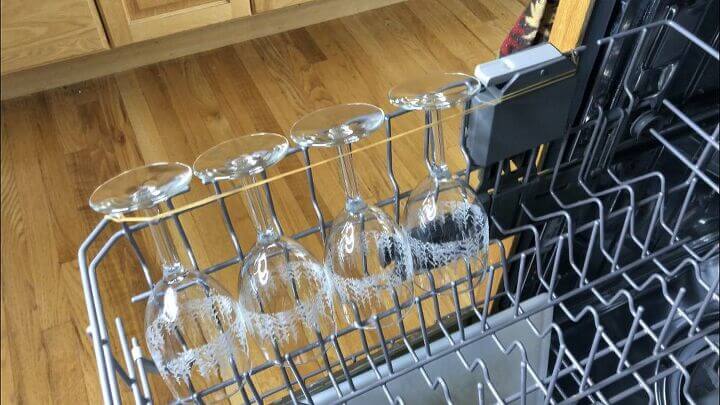 Use a long rubber band by looping it through on one side of your dishwasher, pulling it across the stemware, and hooking it on to the dishwasher via edge or prong.