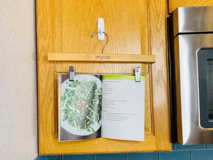 You can use old plastic hangers in your kitchen as well. Place a command hook on your cabinet and then clip your cookbook into place on a pants hanger. Hook this onto your command hook and now you can see your recipes easily without getting them splattered with oil while you're cooking. 