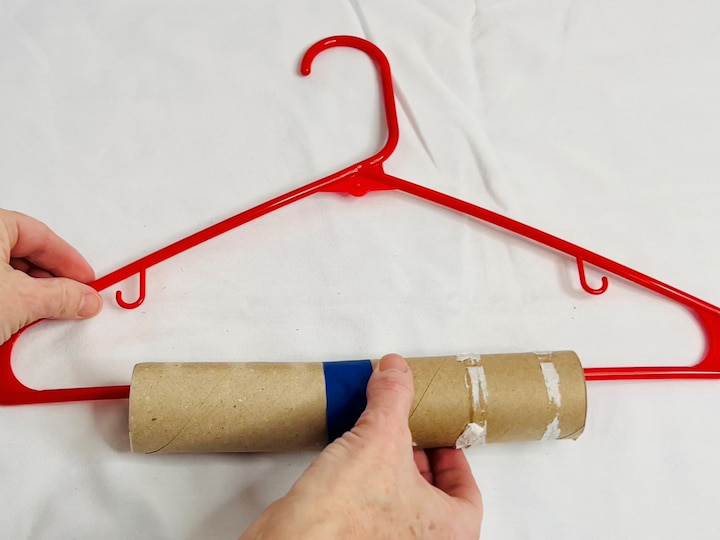 For this next hack, I'm using two toilet paper rolls but you could use a paper towel roll or a pool noodle as well. I'm removing all the paper and cutting a line down the center of each. I am taping them together to make one long roll and I will slip this onto the hanger. When I hang my pants over the top it will prevent the pants from creasing.