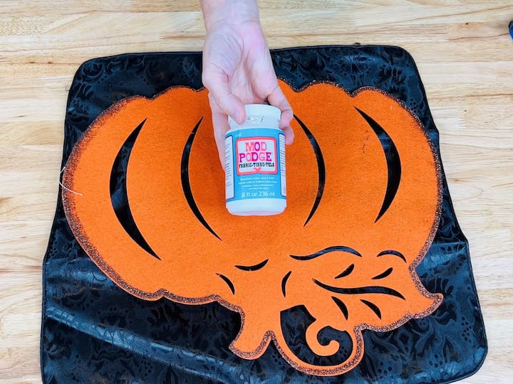 Flip the pumpkin over and use the back side. Dip a paintbrush into fabric Mod Podge and apply a generous coat to the back of the felt pumpkin, ensuring complete coverage.