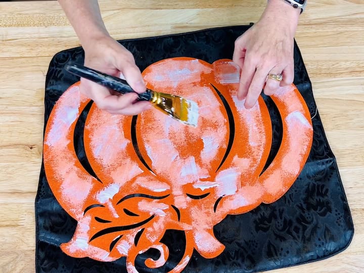 Flip the pumpkin over and use the back side. Dip a paintbrush into fabric Mod Podge and apply a generous coat to the back of the felt pumpkin, ensuring complete coverage.