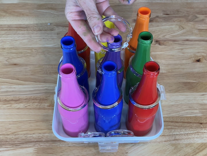 Create a game setup: Choose a suitable base, such as a cupcake holder, crate, or galvanized bucket, to hold the painted bottles. Arrange the bottles in the slots or position them securely.