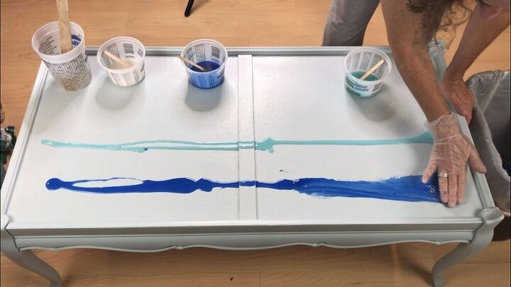 I poured the tinted epoxy onto the coffee table. I started with the true blue in the back, and the ocean view in the middle.  With a glove on my hand, I smeared epoxy over the surface. I also blended the colors together.