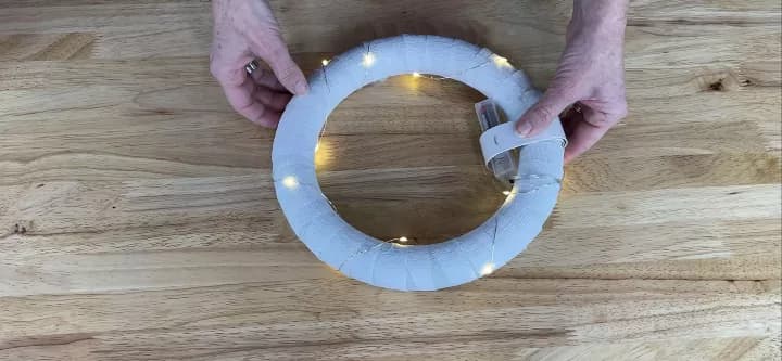 I used a white slap bracelet to hold the battery pack of a LED light strand onto the wreath form.  This would allow me to access the battery pack later to replace the batteries.  I then wound the lights around the wreath form.