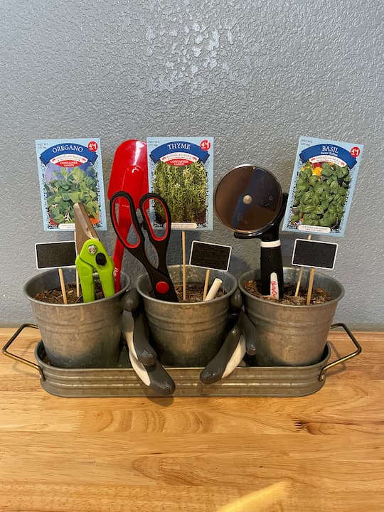 I added the chalk so they would have it for the garden markers.  I added pruners to help care and shape the plants.  I added items that would be helpful in the kitchen to use the herbs like the scissors, pizza cutter, and rubber scraper.  I placed them into the dirt representing flowers or the plant.