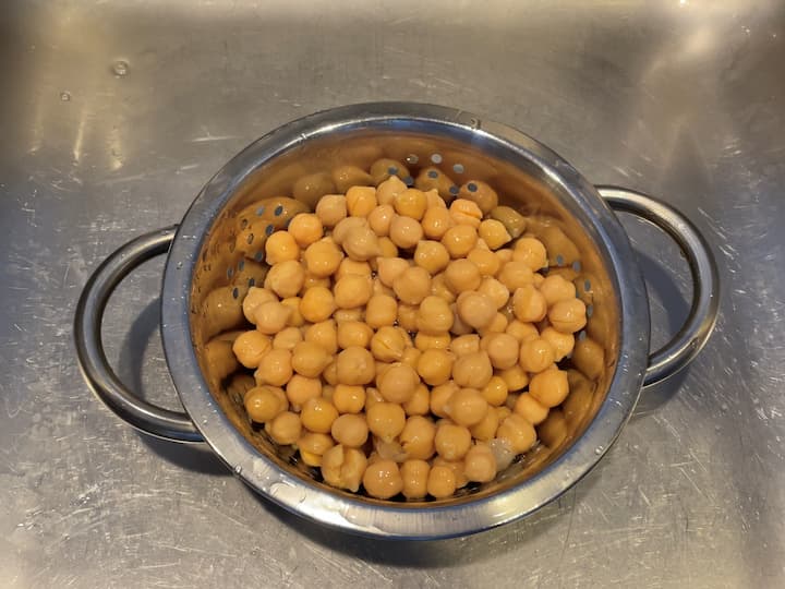 Open one can of garbanzo beans and place in a strainer.  Rinse the chickpeas with water to remove all of the preservative liquid.  Let them sit for a little bit to make sure all the water has drained out.