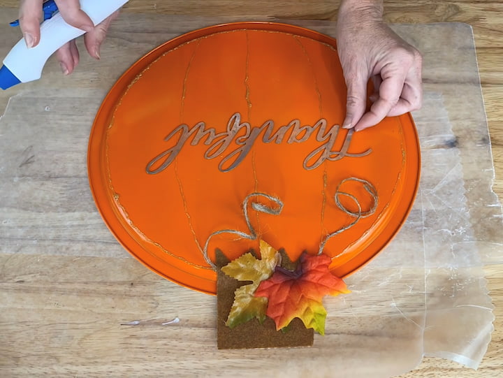 I used a piece of adhesive felt and cut out a stem.  I peeled off just enough backing to stick it on the pizza pan.  I then hot glued on some twine to represent the vine and some faux leaves.  I hot glued on a galvanized word to my dollar tree pumpkin.