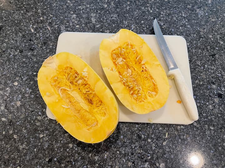 Start by cutting your spaghetti squash in half, and scoop out the seeds and center of the squash.
