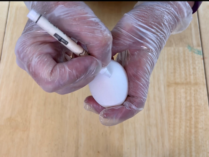 Use a white wax crayon and draw a design on the white egg.  You can use a color crayon but you'll be able to see the design and it won't be invisible.  The waxier the crayon the better it'll work.