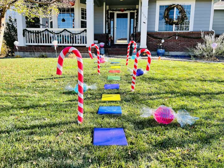 I placed my pavers into the grass forming a walkway to my front door. I placed the candy and lollipop decorations on either side of the walkway. I staked skewers into the ground and added the candy canes to each one, all along the walkway. You might remember these cones that I spray painted for some holiday games, now I'm placing them along my walkway for my Candyland.