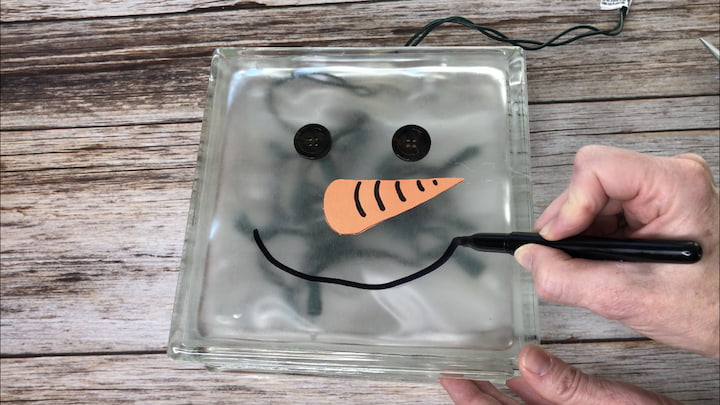I put lights inside the craft block, and I hot glued on 2 buttons for eyes.  I cut a carrot nose out of construction paper, drew on the lines for definition, and hot glued that on to the bock.  I drew on a mouth with a permanent marker.