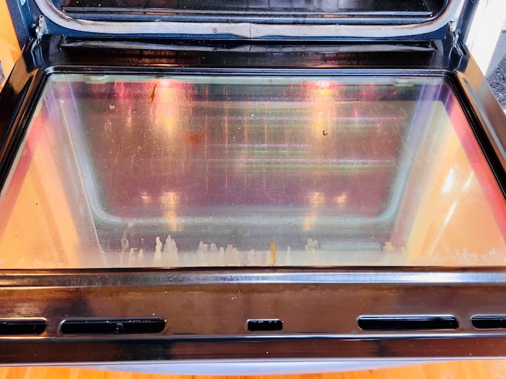 Here is how to clean oven glass. Now here you can see all of the grease and yuck on the inside of my oven door window. All you need to do is take a damp eraser and it cleans all of that grease right off super easily.