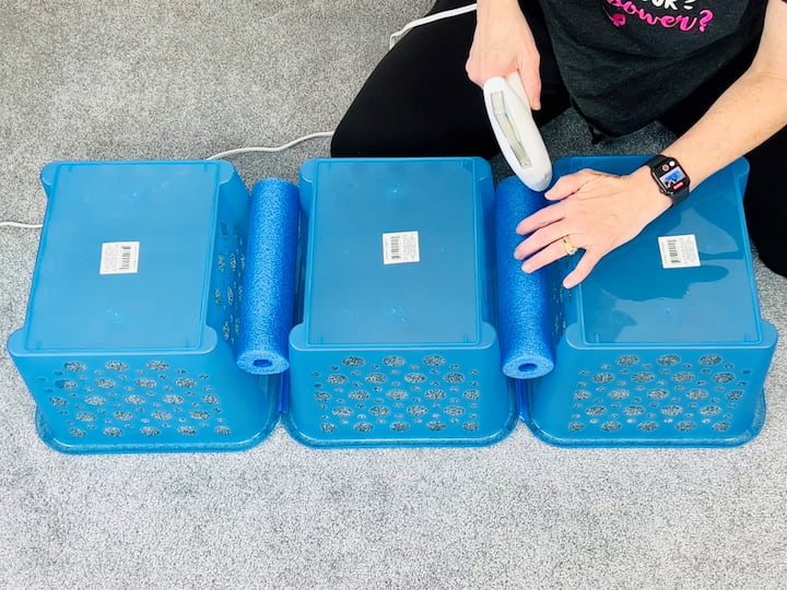 Next, grab your hot glue gun.  I'm using my Xyron self-loading glue gun, which is super awesome, to hot glue each of the pool noodles into place between each of the baskets.  This helps make them more stable.   I repeated the process and made two sets of baskets.   