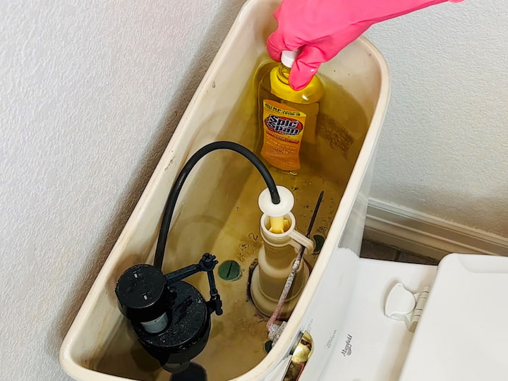 Poke a small hole or two in a bottle of Spic and Span container with a sharp object. Remove the lid from the top of your toilet tank and place the container inside. Place the lid back on, and let the cleaner leak out to clean your tank and toilet. If you don't like harsh chemicals, you can also use a Castile soap bottle or vinegar.