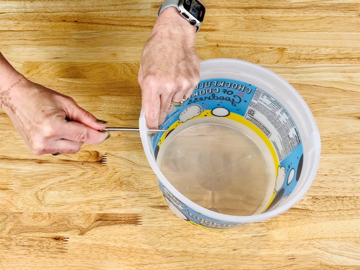 Remove the handle from the ice cream bucket and poke a hole on either side of where the handle was.