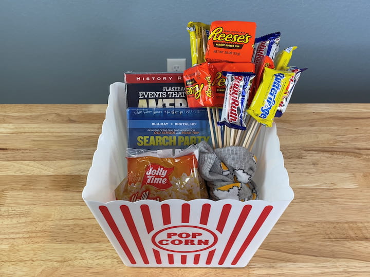 Tape the snacks onto the skewers. Stick the skewers into one of the socks to make a candy bouquet. Wrap the other sock around the bouquet and tie it into place. Assemble the gift by placing the popcorn, movies, and candy bouquet inside the basket.
