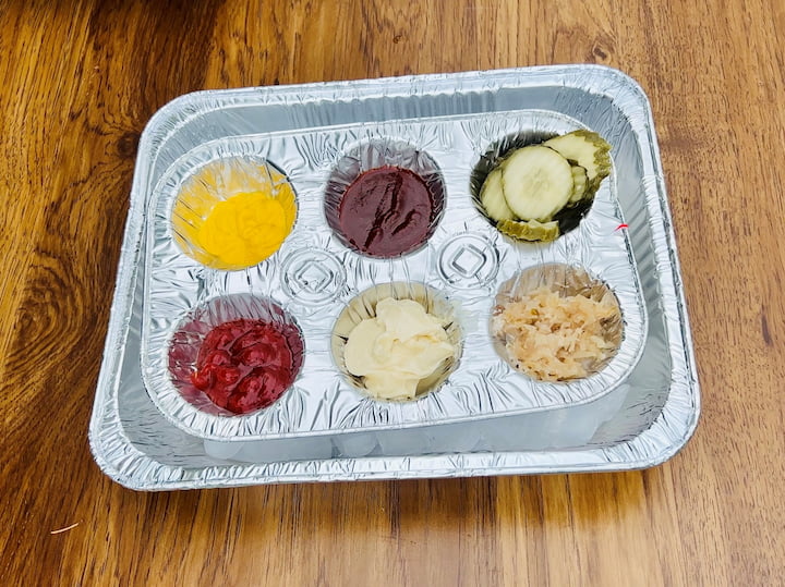 Use a muffin tin to organize and display your condiments. It keeps them neatly separated and easily accessible for your guests. For keeping them cool, grab two lasagna pans from the dollar store. Fill one half with ice and place your condiment-filled muffin tin on top. This setup ensures that your condiments stay nice and chilled for your backyard barbecue.