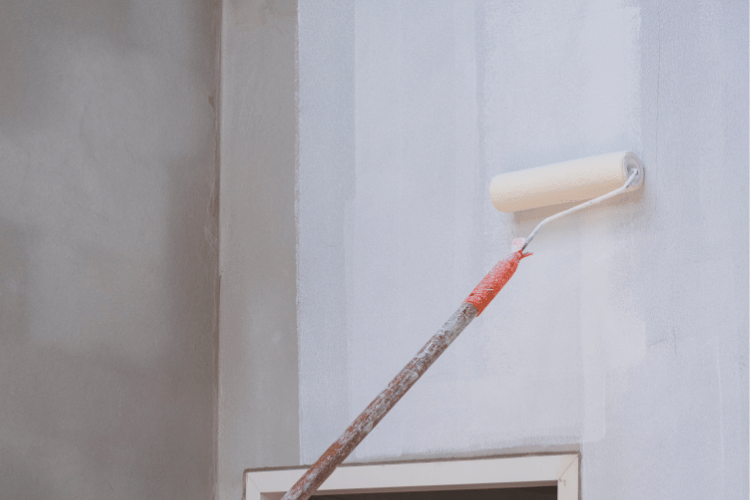 Long handle roller brush applying primer white paint with door frame on cement wall