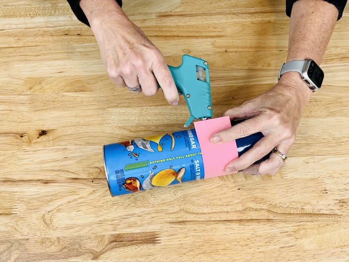 Measure the middle section to become the face with pink construction paper, cut the paper, and then glue it underneath the blue vinyl on the chip can.