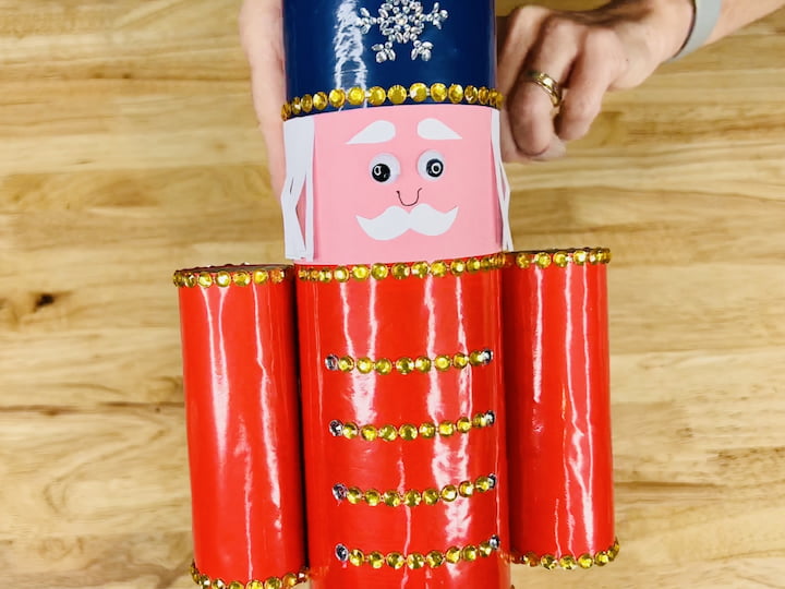 Add google eyes, eyebrows, a mustache, and a nose to create a face.Craft a hairpiece by cutting and folding white paper.Glue the hairpiece onto the chip can to complete your nutcracker.