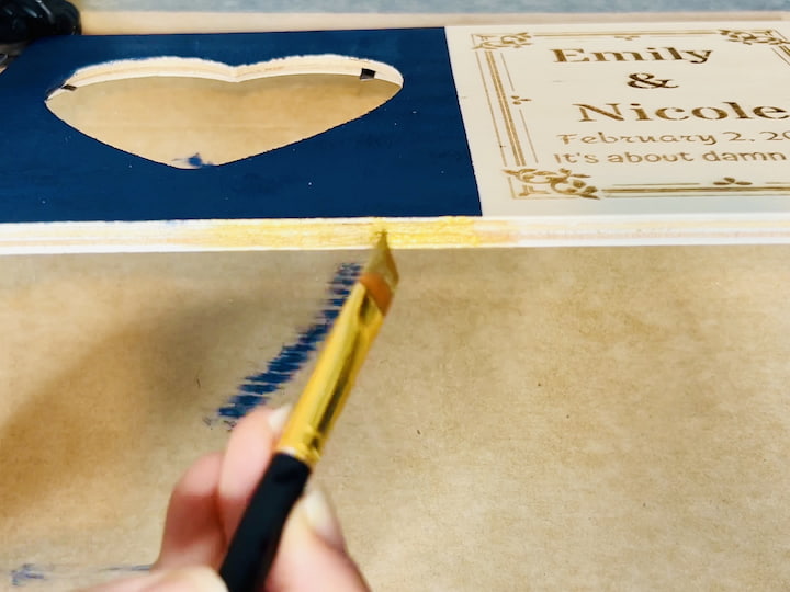 Step 2: Adding Treasure Gold Accents For an elegant touch, incorporate Folk Art Treasure Gold into the design. Paint the edges, including the top, bottom, and sides, as well as the edges within the heart engraving. This gold accent will enhance the overall aesthetic and tie in with the wedding colors. Take your time to ensure even coverage and precise detailing.