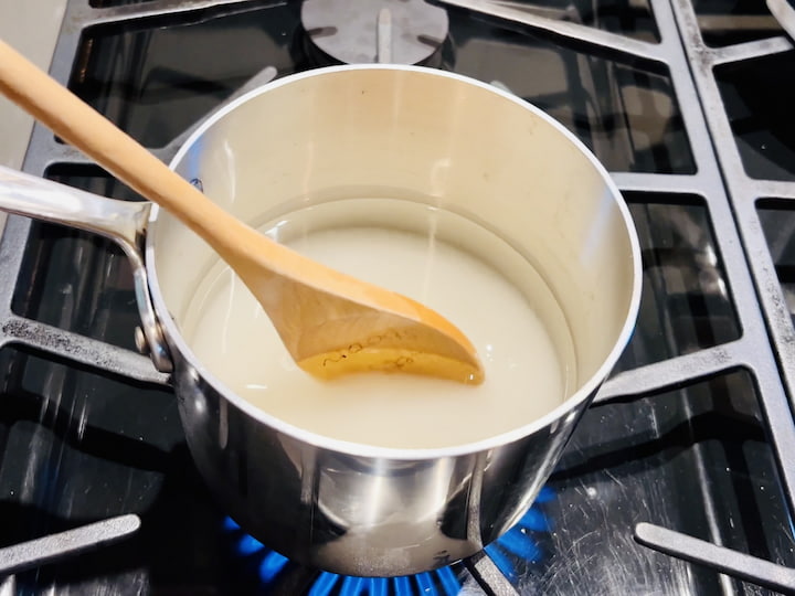 Start by placing two cups of water into a medium saucepan. Add two cups of sugar into the water and stir continuously over heat until the sugar is completely dissolved. This process creates a sweet and glossy simple syrup.