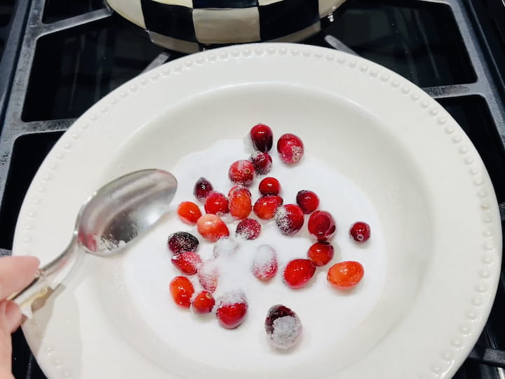 After the soaking period, place some sugar into a bowl. Scoop out the cranberries from the simple syrup with a slotted spoon and toss them in the sugar until they are fully coated. This step adds an extra layer of sweetness and texture.