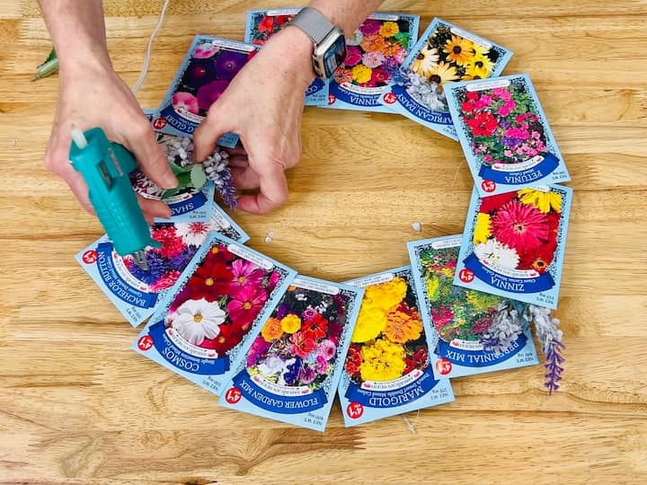 overhead shot showing flowers being hot glued between some of the seed packets on wreath