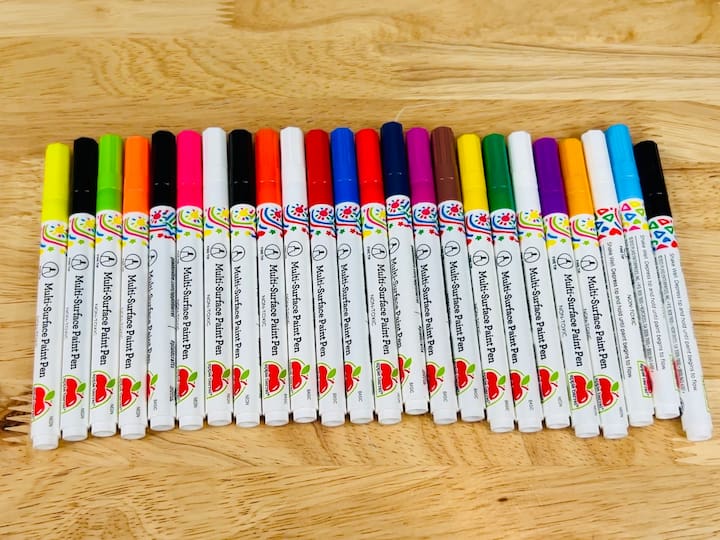 overhead shot of multi surface paint pens lined in a row with twenty four colors on wooden table