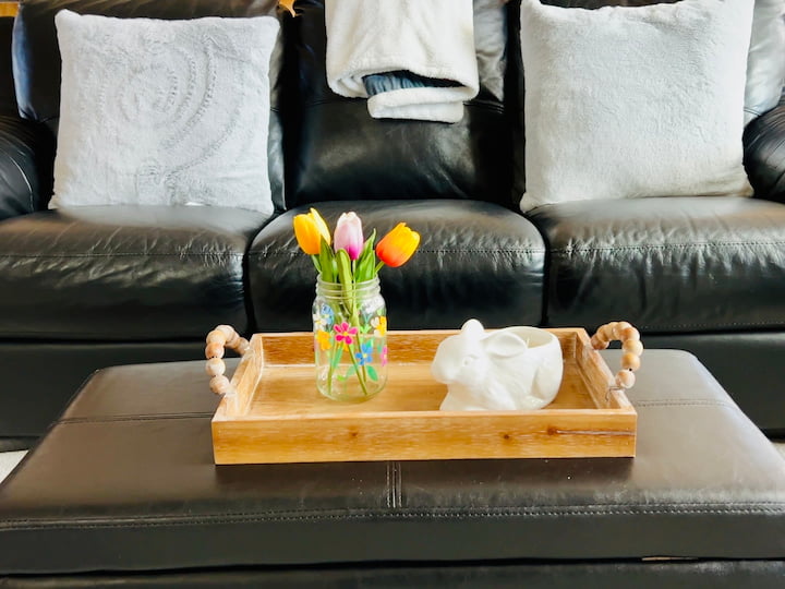 flower craft vase holding tulips on a serving tray on ottoman with a couch in background