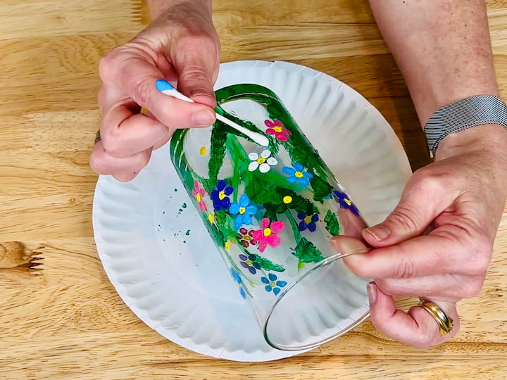 overhead shot of flipped qtip painting white flower petals like a daisy on the flower craft vase. 