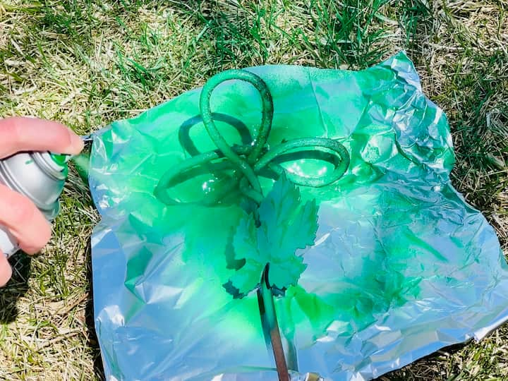 Repurposed candle holder being spray painted with green Rustoleum spray paint. 