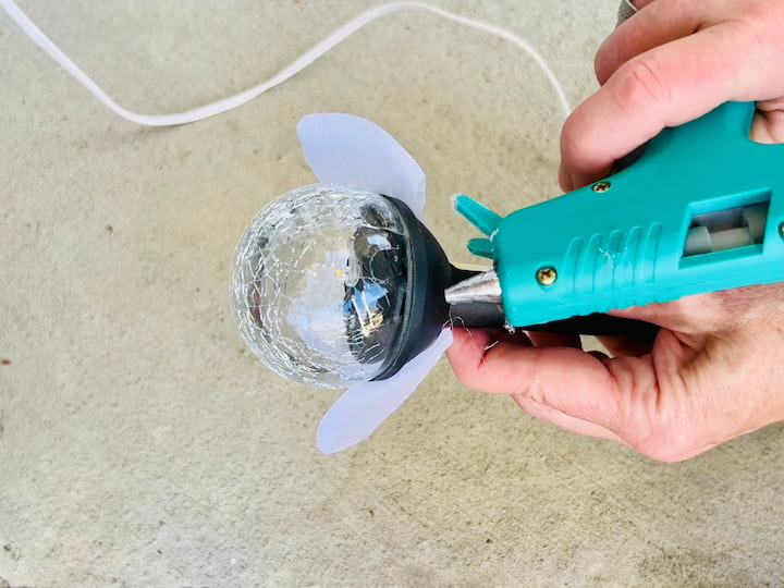 I warmed up my cool glue gun, and I put a dab of cool glue onto the solar light. Then I placed the petal onto the dab of glue.