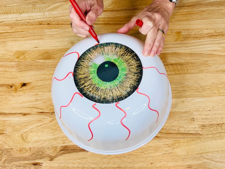 I started by hot gluing the eyes onto the bottom of the white bowls. And then I took a red permanent marker and made squiggle lines all along the white bowl to make the eyeball. And I made two of these. 