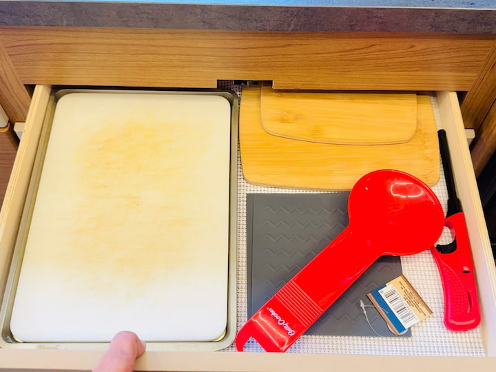 The DIY: I found that a simple baking sheet from Dollar Tree fits perfectly! This acts as a base and protects the wood.

What I Store: Small items like a thin cutting board, pot holders, and a clicky lighter (since this drawer is conveniently located near the stove).